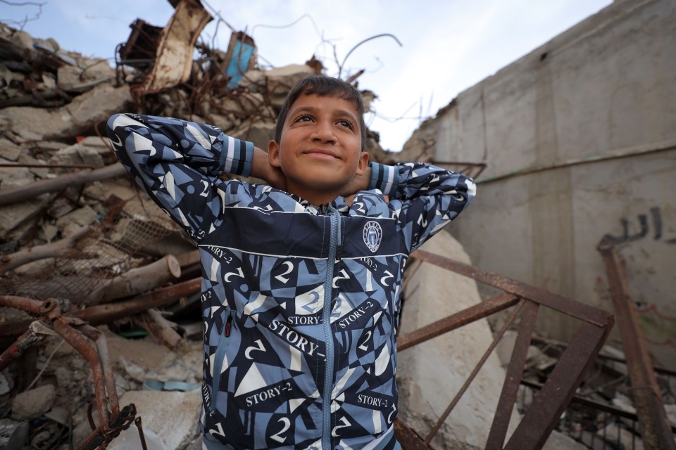 Boy in patterned jacket amidst rubble.