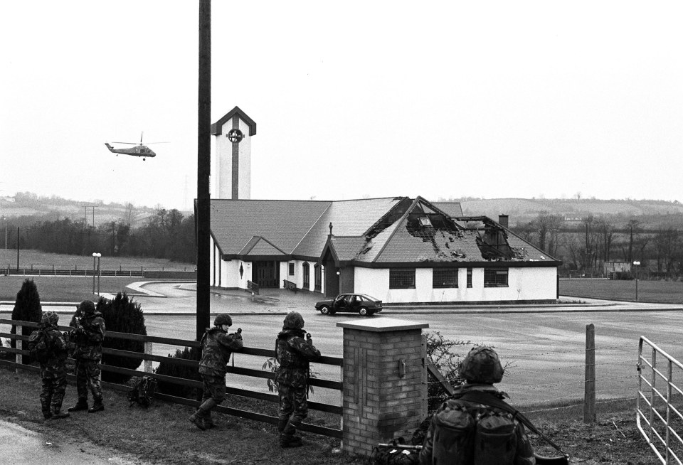 Aftermath of an IRA shooting; soldiers stand guard near a damaged building and abandoned vehicles.