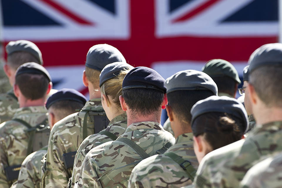 British soldiers standing in formation with a Union Jack flag in the background.