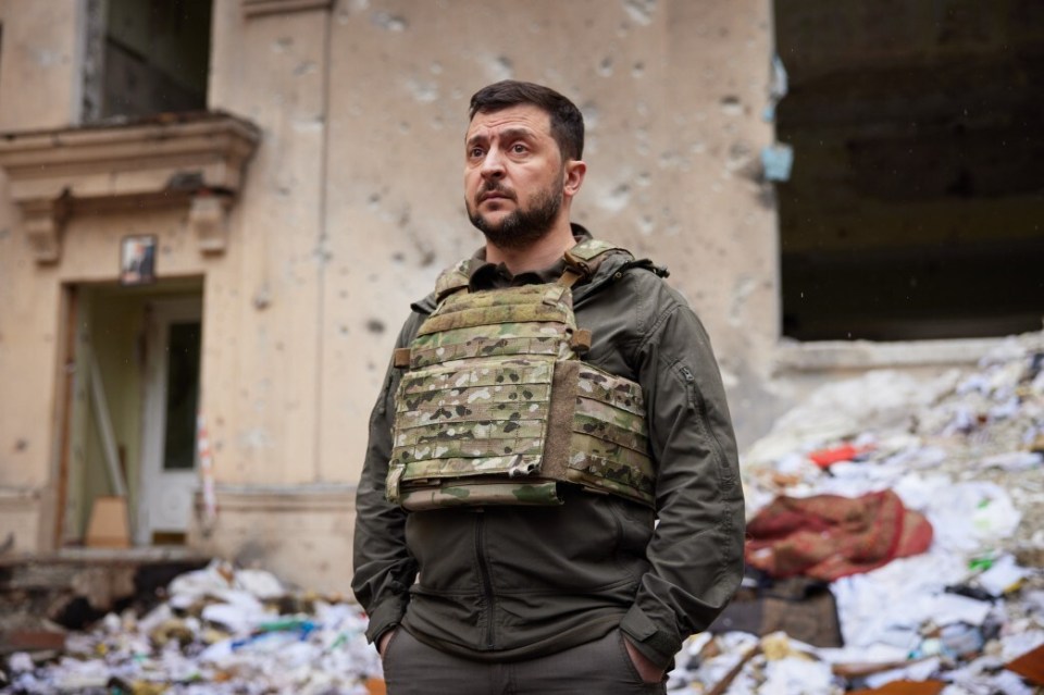 Volodymyr Zelenskyy in body armor amidst war-damaged buildings.