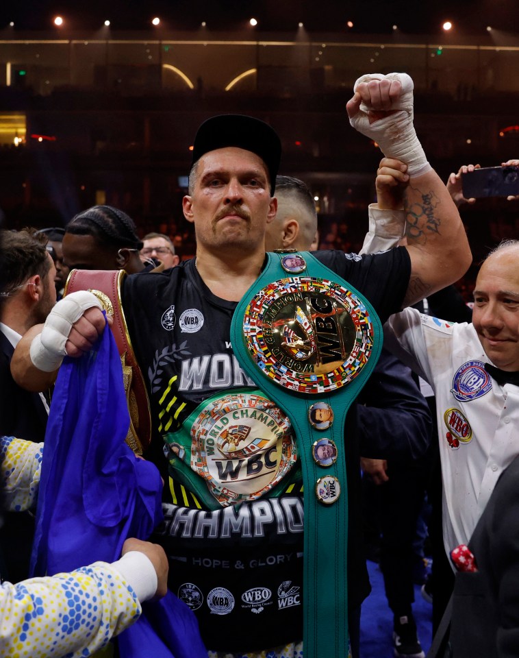 Oleksandr Usyk celebrates with championship belts after a boxing match.