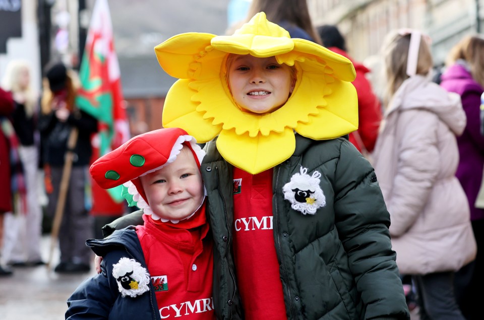 Two children in daffodil and dragon costumes at a Welsh market.