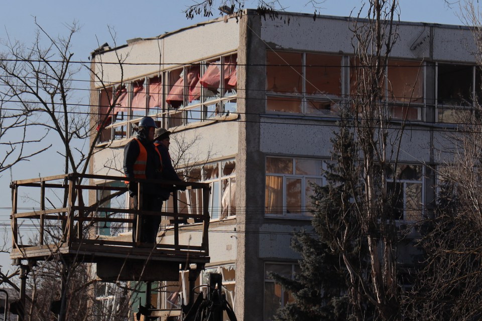 Two workers on a lift platform survey damage to a hospital building.