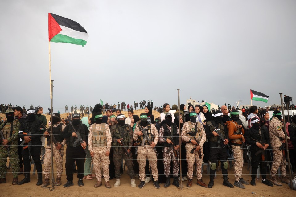 Hamas fighters stand behind a fence at a handover of Israeli hostages' bodies.