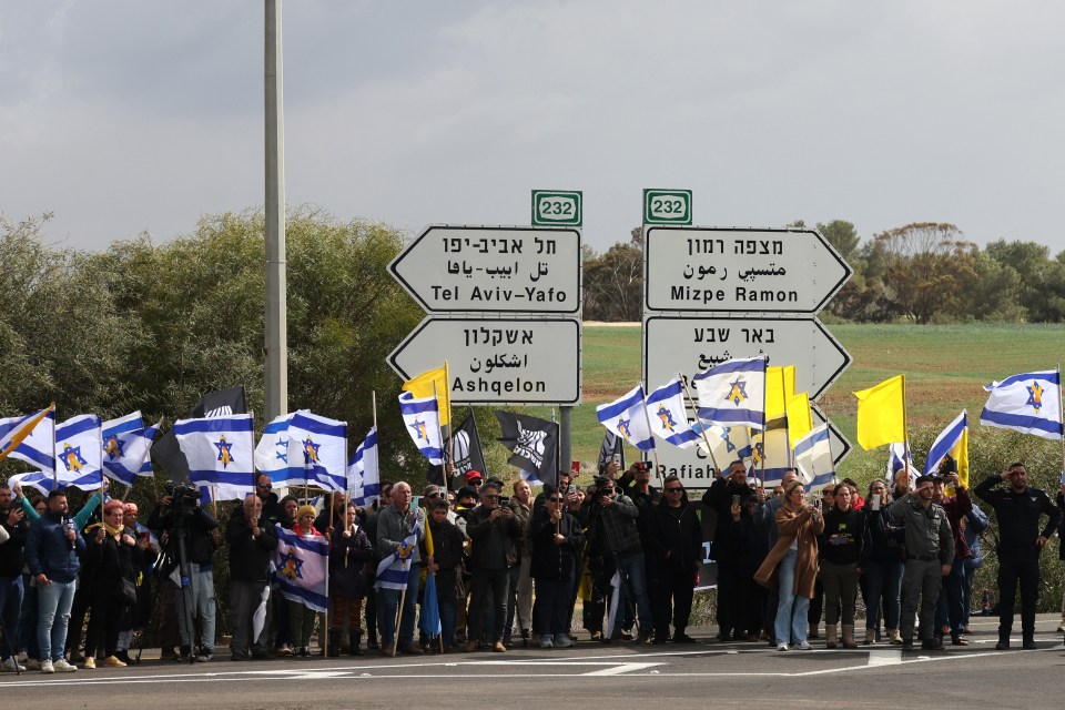 Israelis waving flags await the handover of hostages' bodies.