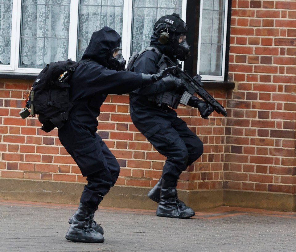 Two bomb disposal officers in protective gear and gas masks.