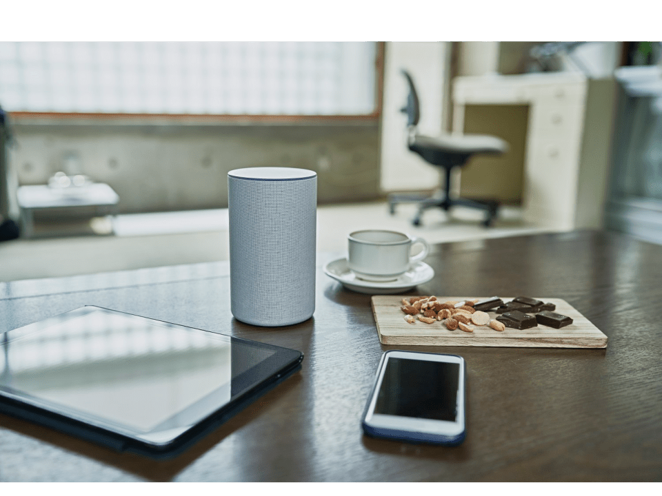 Smart speaker, tablet, phone, nuts, and chocolate on a table.