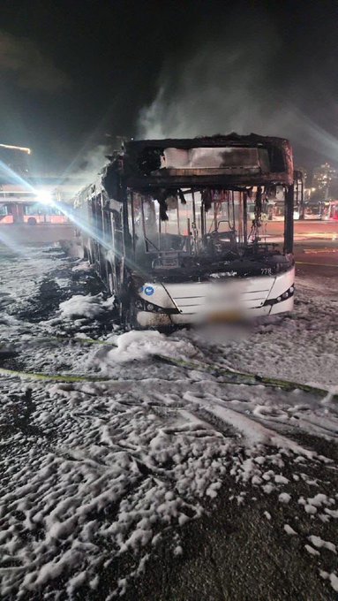 Burned-out bus covered in fire suppressant foam.