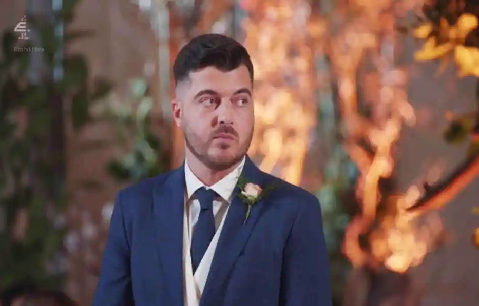 A man in a blue suit looks pensively to his side.