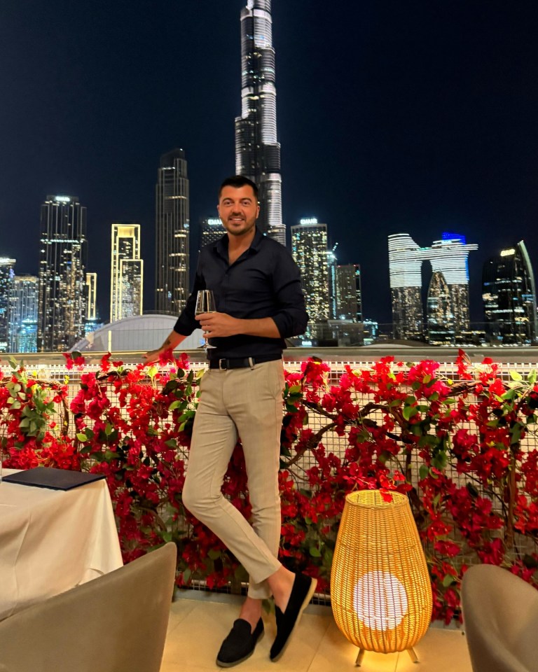 Man holding wine glass on a rooftop terrace overlooking Dubai skyline.