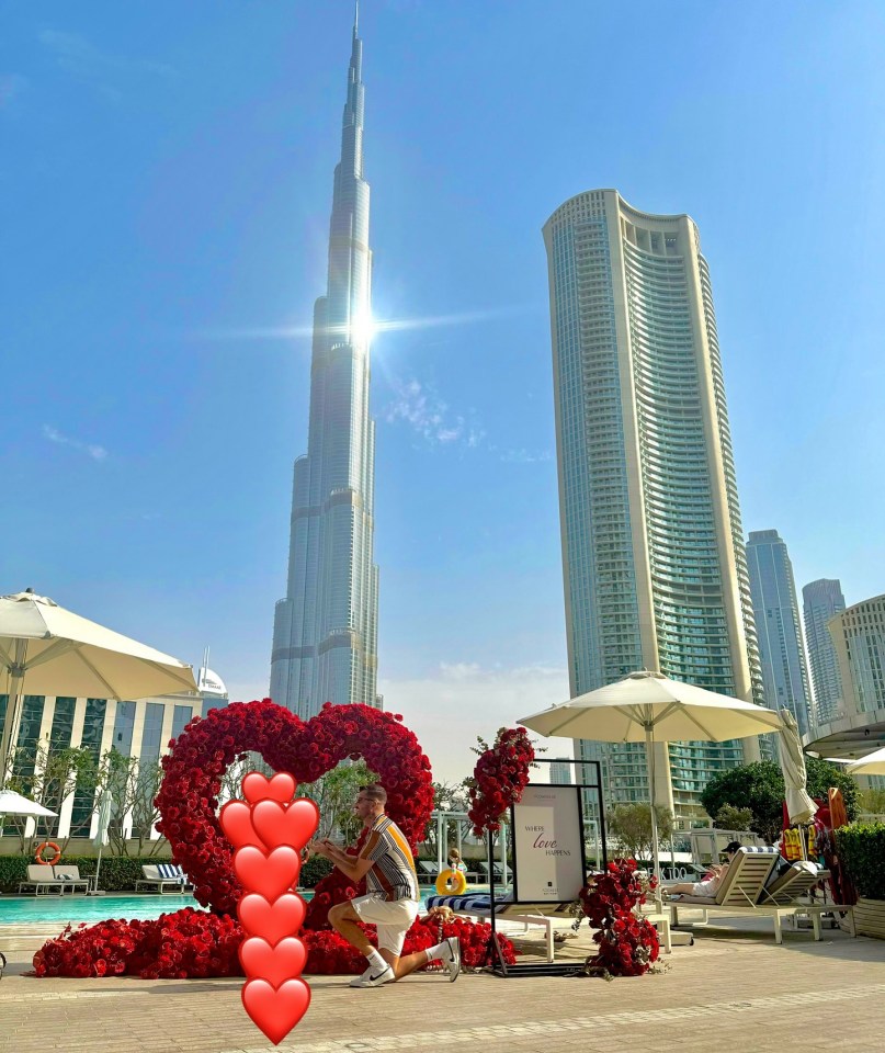 Man kneeling by a heart-shaped rose display in front of skyscrapers.