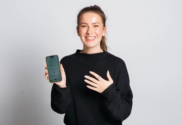 Woman smiling and holding up a smartphone displaying a fertility tracker app.
