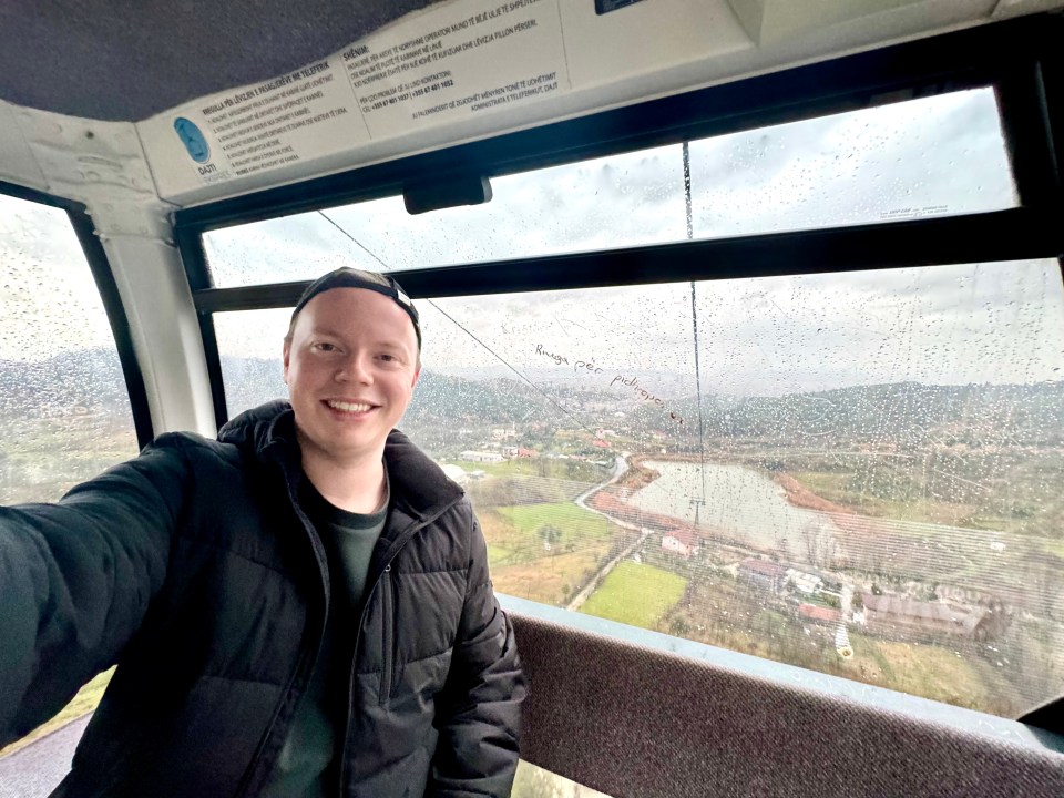 Selfie of a man in a cable car overlooking a rainy landscape.