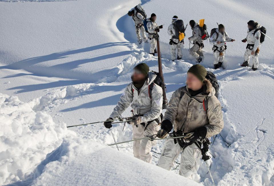 Soldiers rappelling in snowy mountains.