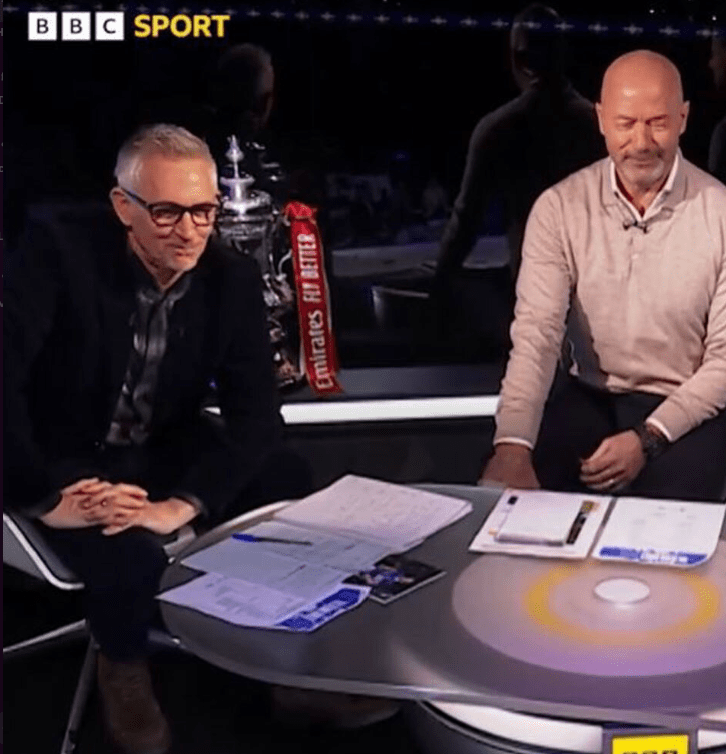 Two men sitting at a desk discussing sports.