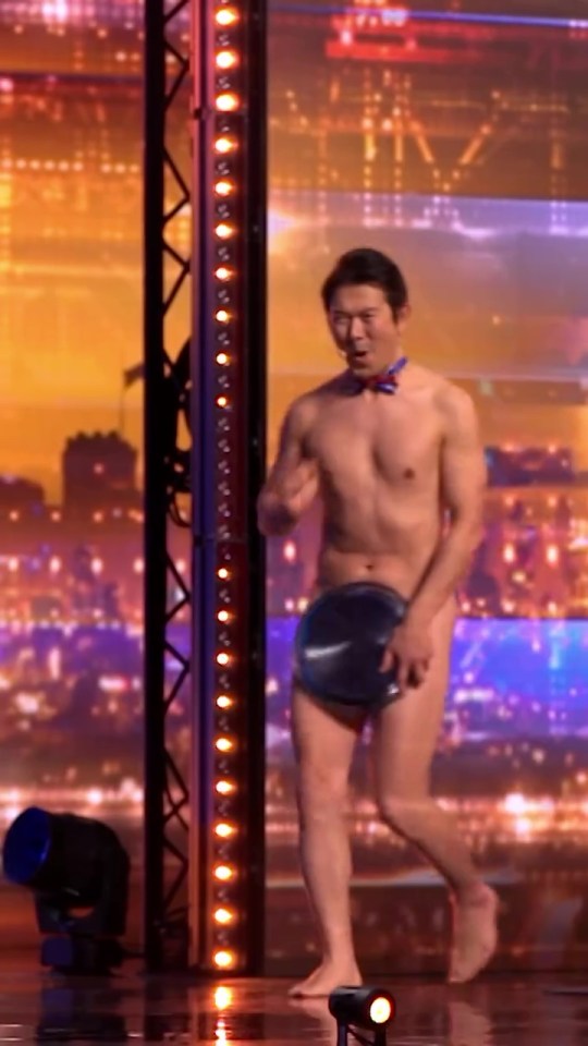 A shirtless man with a bow tie holds a plate on a stage.