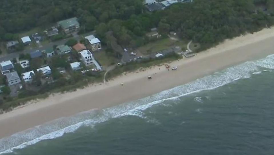 Aerial view of a beach with houses and emergency vehicles.