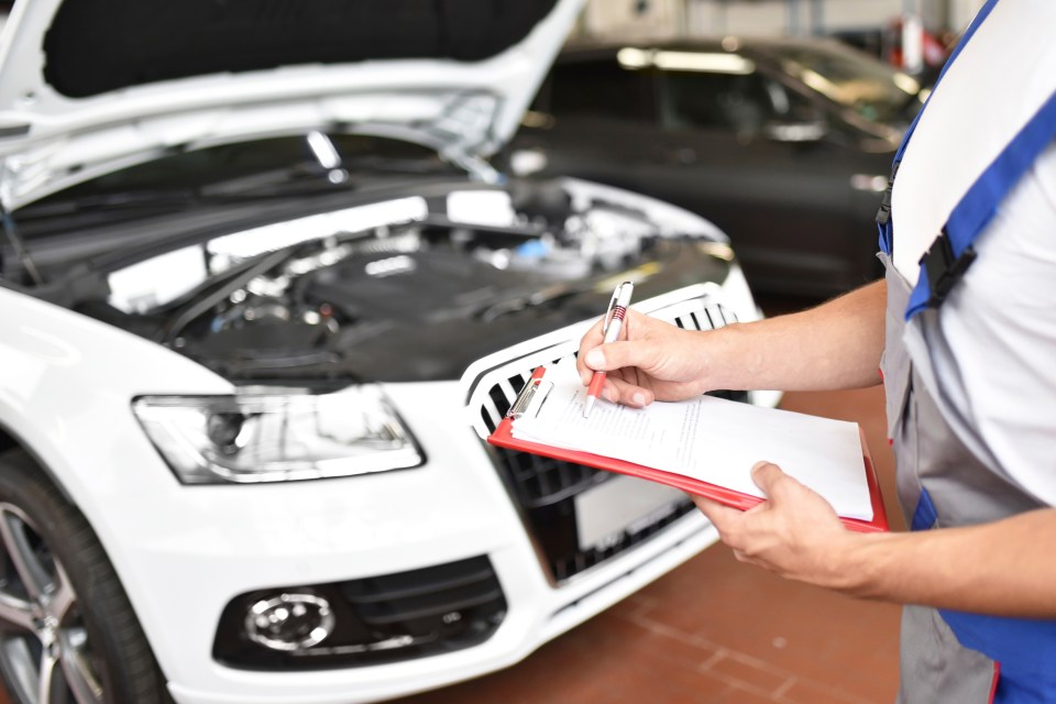 Mechanic filling out a clipboard next to a car.