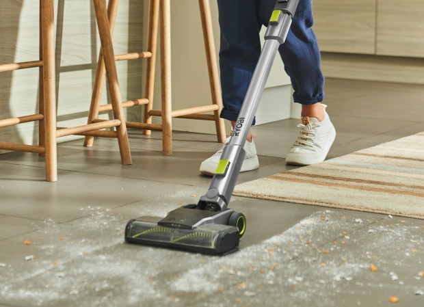 Person using a Ryobi cordless stick vacuum to clean a floor.