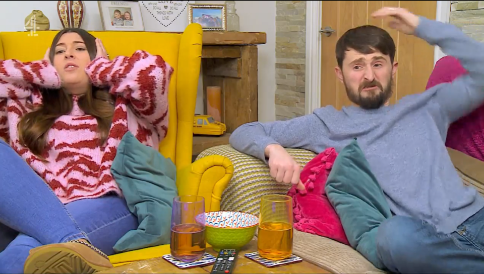 A man and woman sitting on a couch, looking stressed.