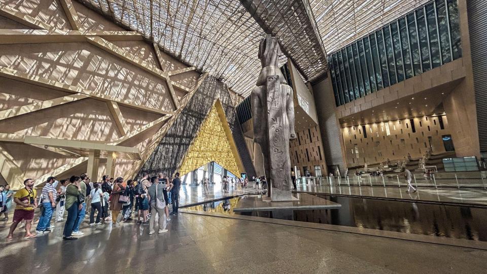 Grand Egyptian Museum interior with a large statue and visitors.