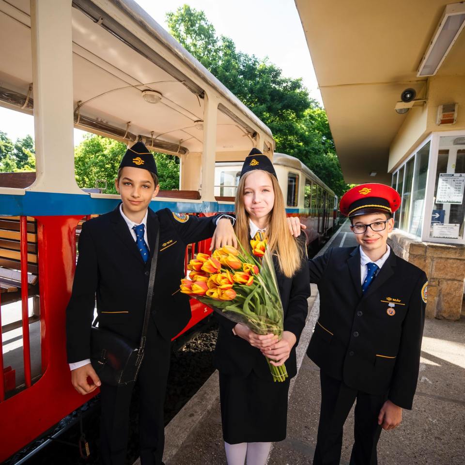 Three children in uniform holding tulips at a train station.