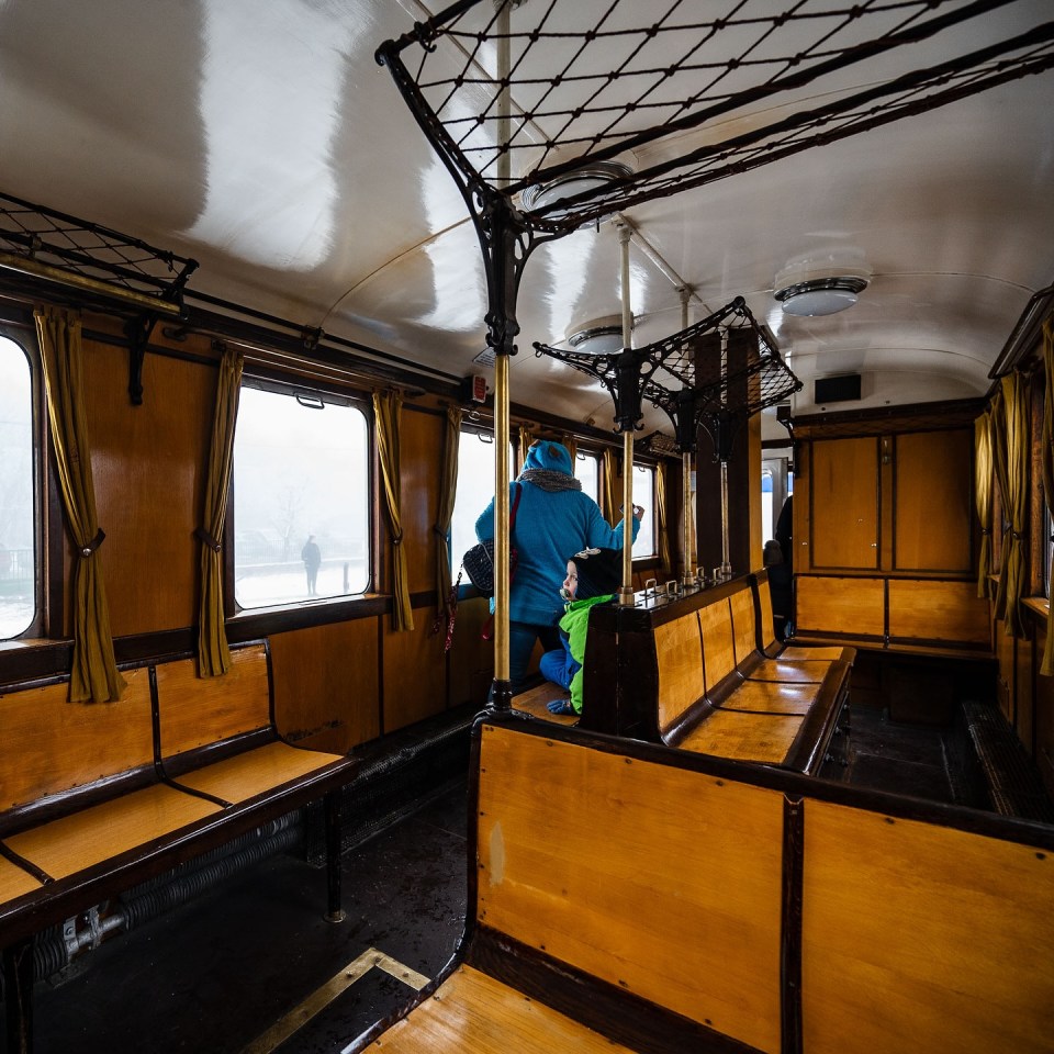 Interior of a quaint Hungarian railway car with wooden benches and passengers.