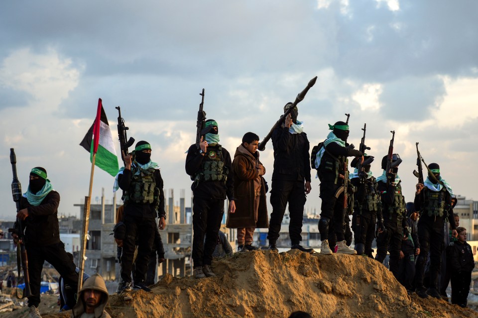 Hamas fighters with weapons and a Palestinian flag stand on a mound of earth.
