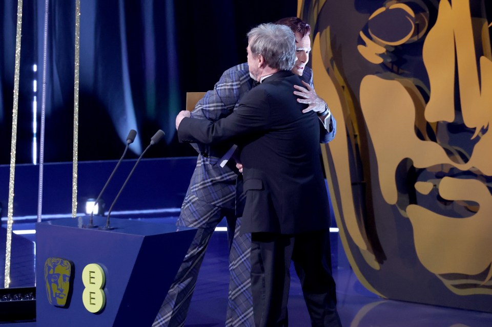 David Tennant and Mark Hamill hugging on stage at an awards ceremony.