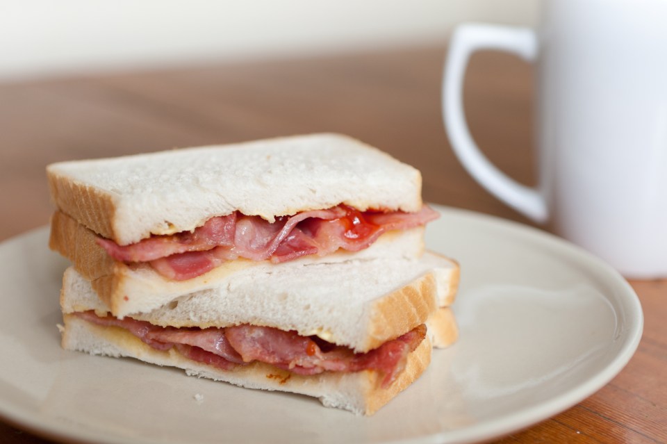 Bacon sandwich with ketchup and a cup of coffee.