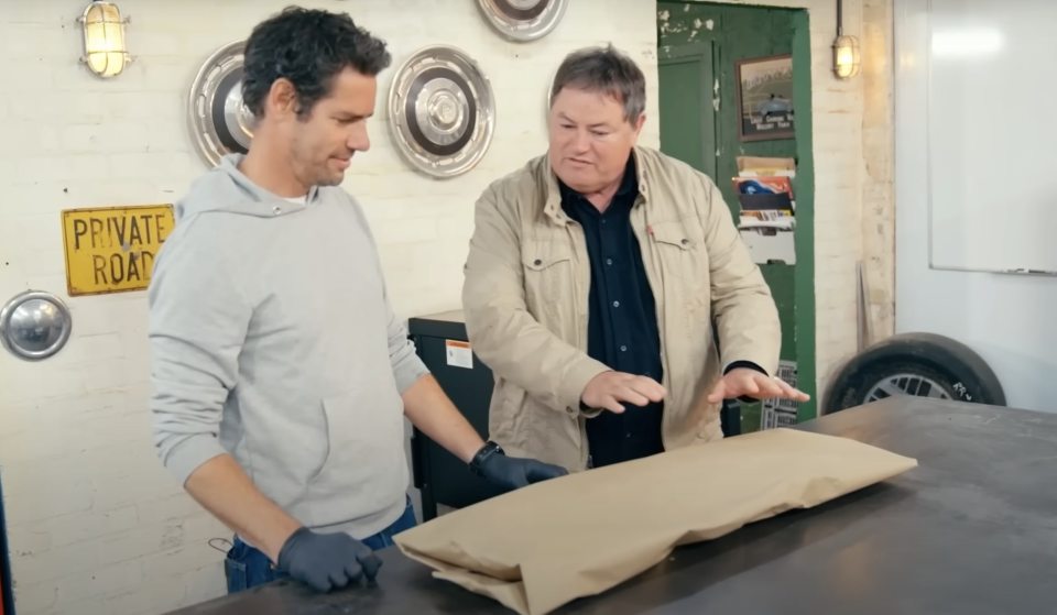 Wheeler Dealers hosts Mike Brewer and Elvis Priestley unveil a car part.