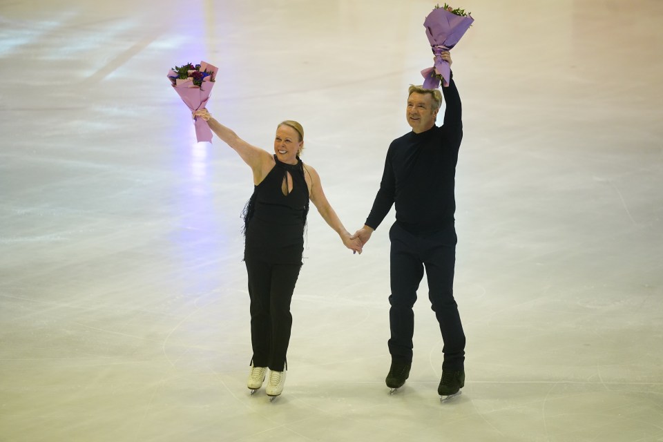 Jayne Torvill and Christopher Dean on ice skates, holding bouquets of flowers.
