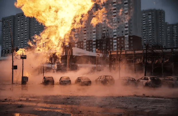 Large fire engulfing a city street with several cars submerged in smoke and water.