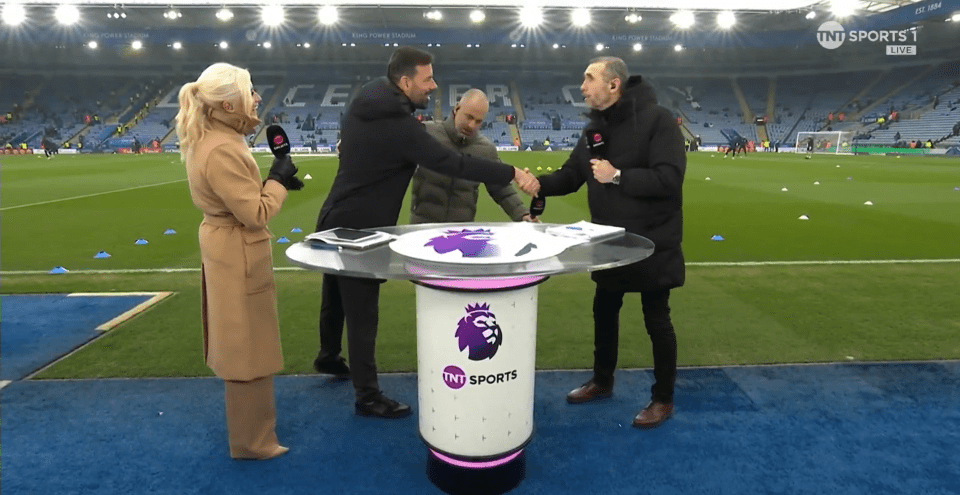Three sportscasters at a soccer field, shaking hands near a table with a microphone and logo.