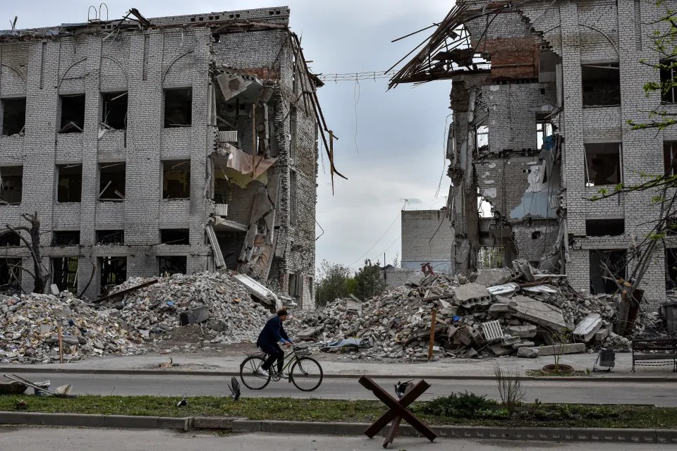 Person on bicycle in front of bombed-out buildings.
