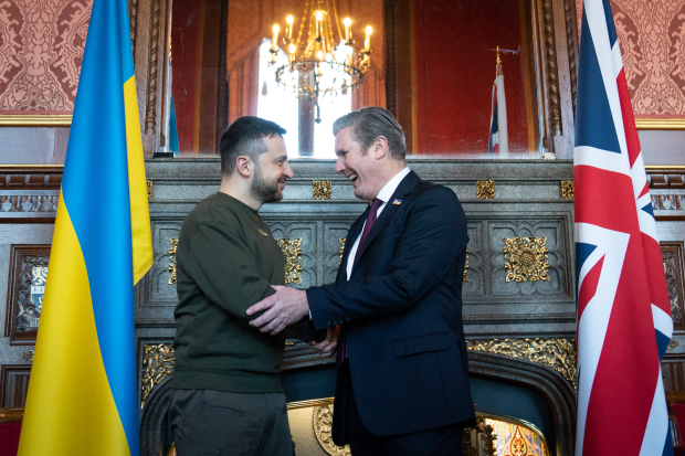 Two men shaking hands, smiling; Ukrainian and UK flags in background.