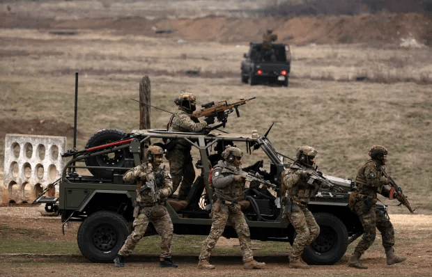 Soldiers with rifles disembarking from a military vehicle.