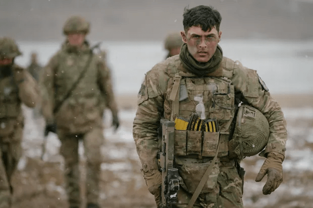 Soldier in camouflage carrying a rifle and helmet.