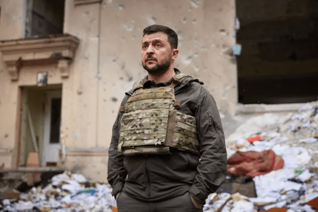 Volodymyr Zelenskyy in body armor amidst war-torn surroundings.