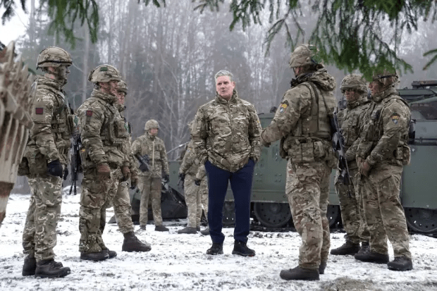 A man in civilian clothes speaks with soldiers in camouflage uniforms in a snowy field.