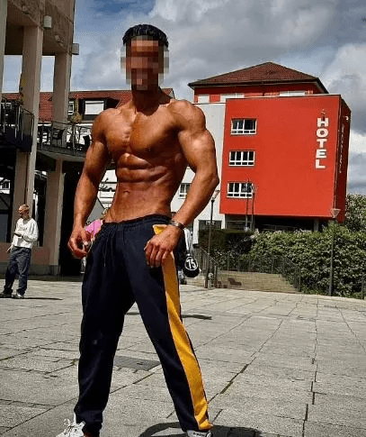 Muscular man in athletic pants standing outside a hotel.