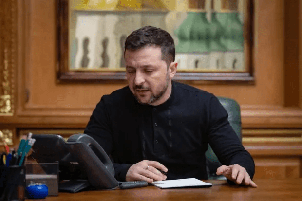 A man sits at a desk, reviewing a document and using a telephone.