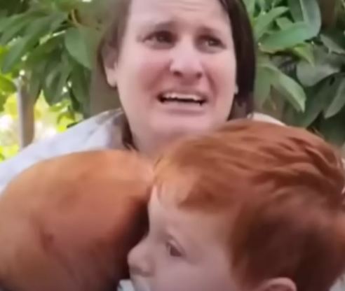 Woman holding two young children, crying.