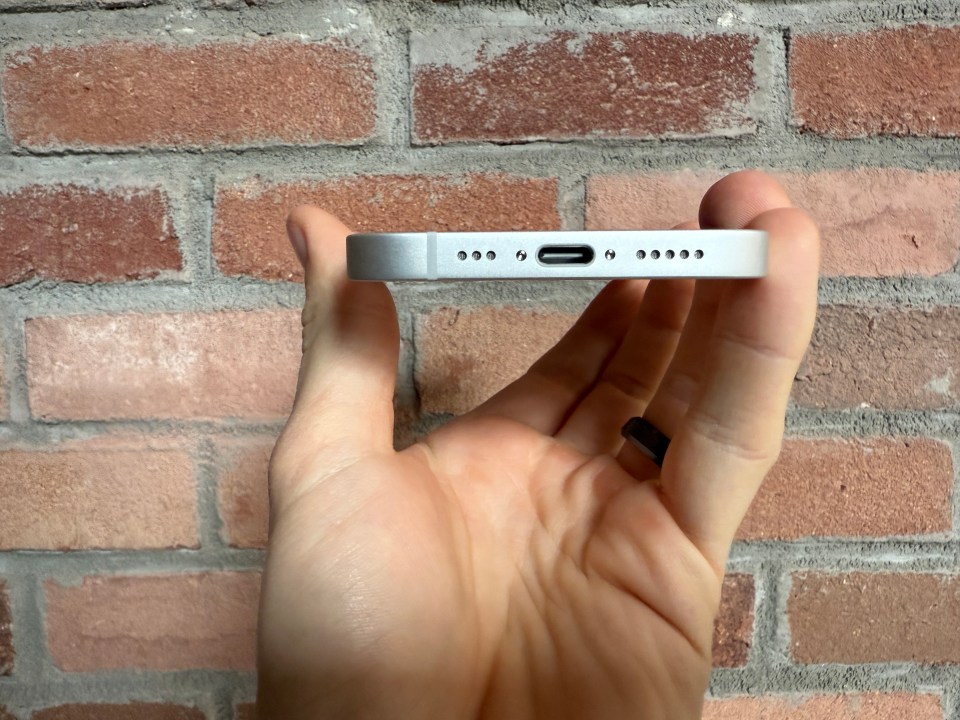 Hand holding a phone, showing the bottom edge with ports and speakers.