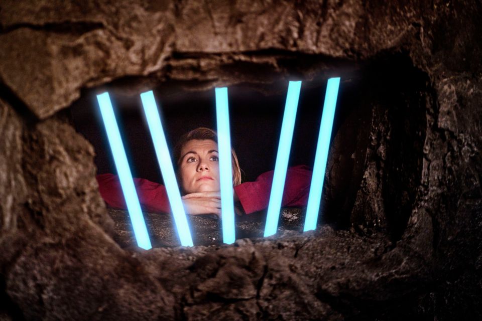 Jodie Whittaker as the Doctor in Doctor Who, peering through bars.