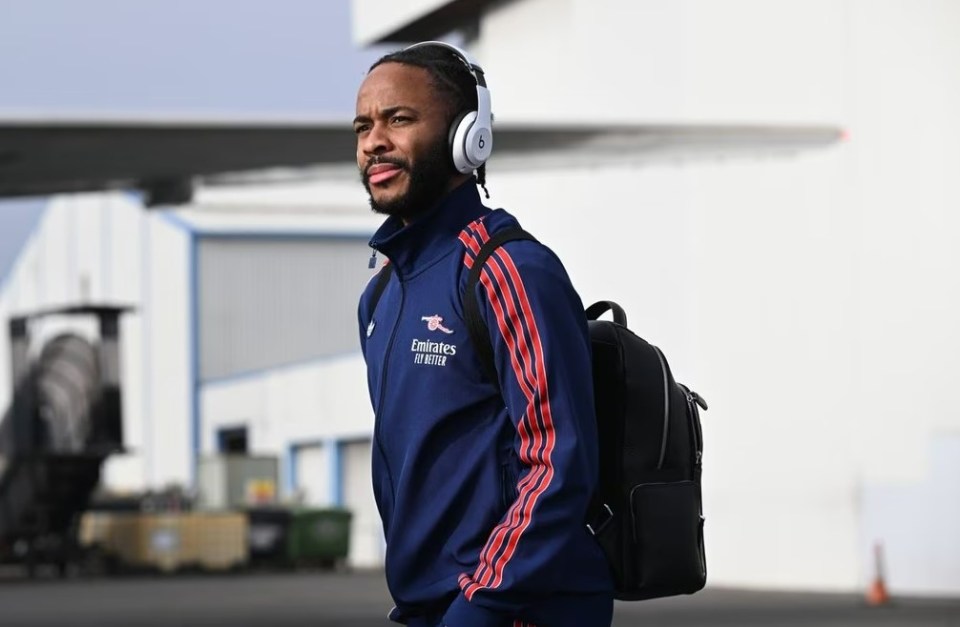 Arsenal player wearing team jacket and headphones at an airport.