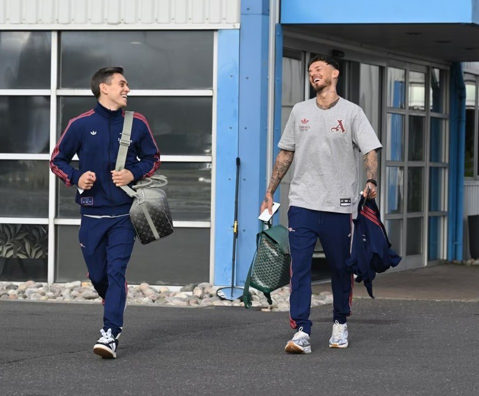 Two Arsenal players walking and carrying bags.