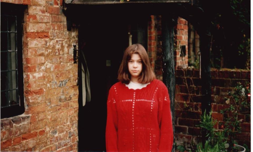 Photo of a girl in a red sweater standing in front of a brick building.