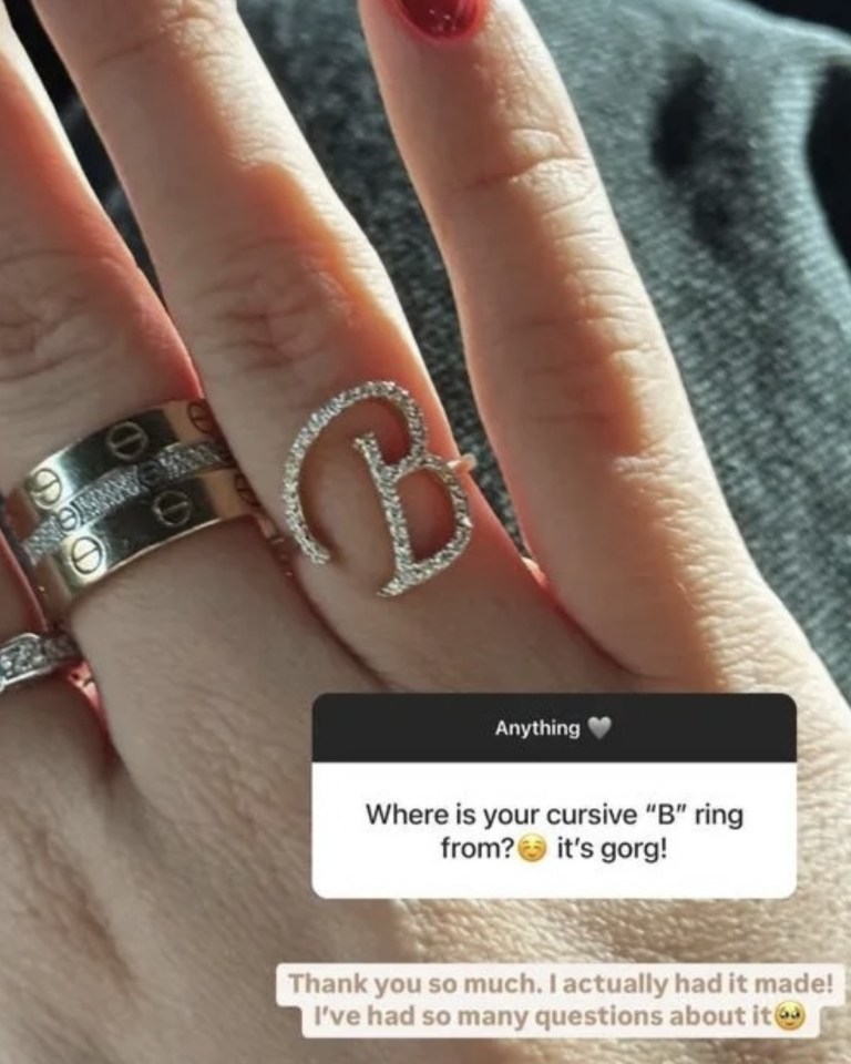 Hand wearing a cursive "B" ring and other rings.
