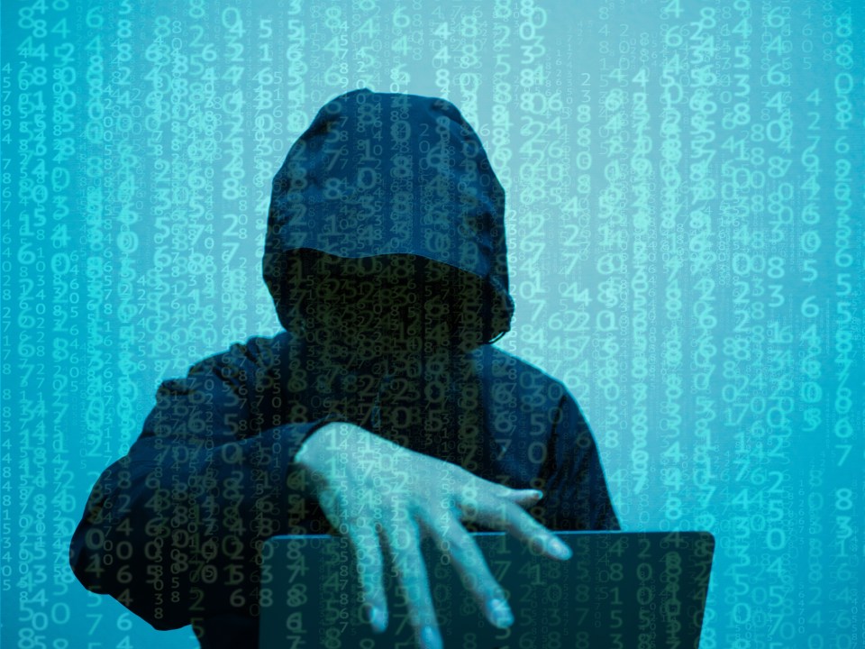 Hooded figure using a laptop, obscured by a background of cascading numbers.